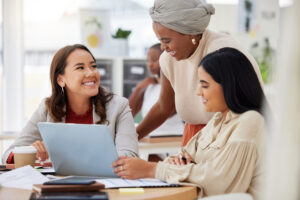 An all-women medical affairs team are gathered around a computer, smiling at each other.