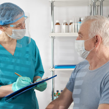 A female physician is taking the medical history of an older, male clinical trial participant.