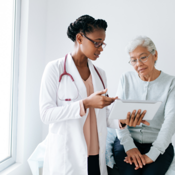 A female doctor in a white coat is talking to a female patient advocate