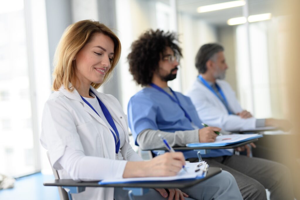 Three healthcare professionals, including one young woman, a young man, and and older man, are attending a medical education event and taking notes.