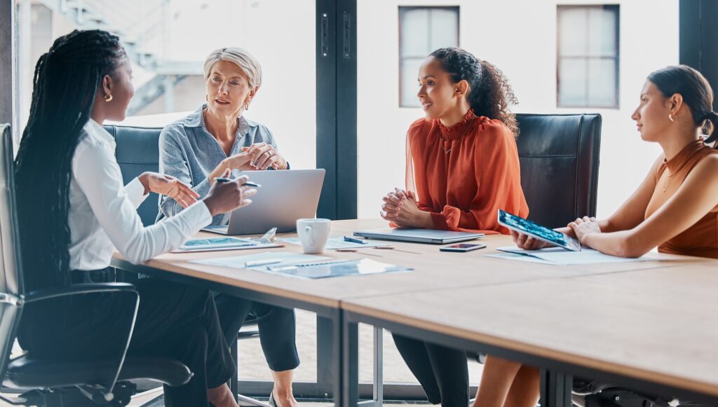 Four women in business clothing are sitting around a rectangular table.
