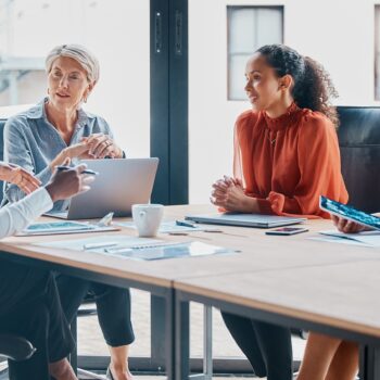 Four women in business clothing are sitting around a rectangular table.